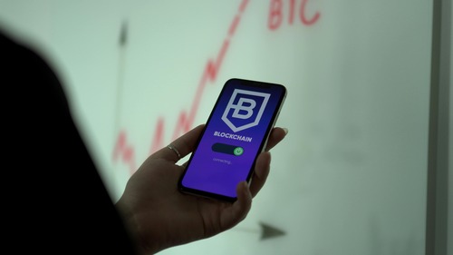 Hand holding a smartphone showing a blockchain wallet app with a rising BTC price chart