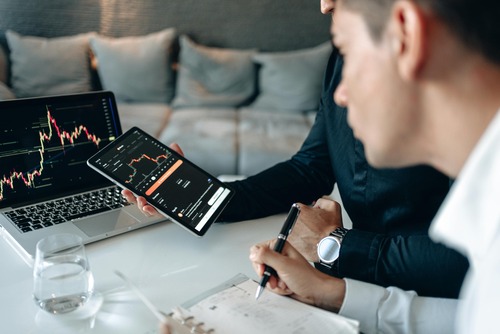 Two people reviewing cryptocurrency exchange rate charts on a laptop and tablet