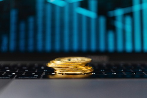 Stack of gold cryptocurrency coins on a laptop keyboard with a rate chart in the background